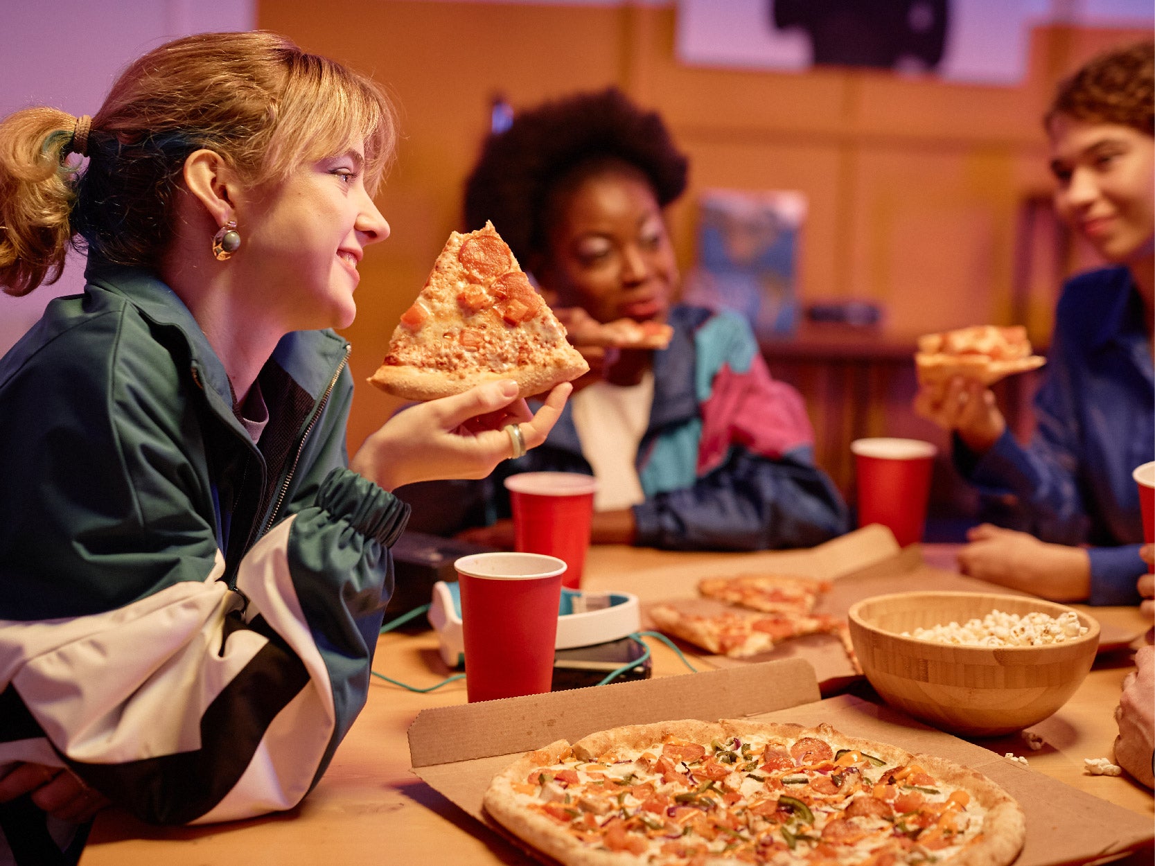 A group of young people smile while eating pizza at a table.