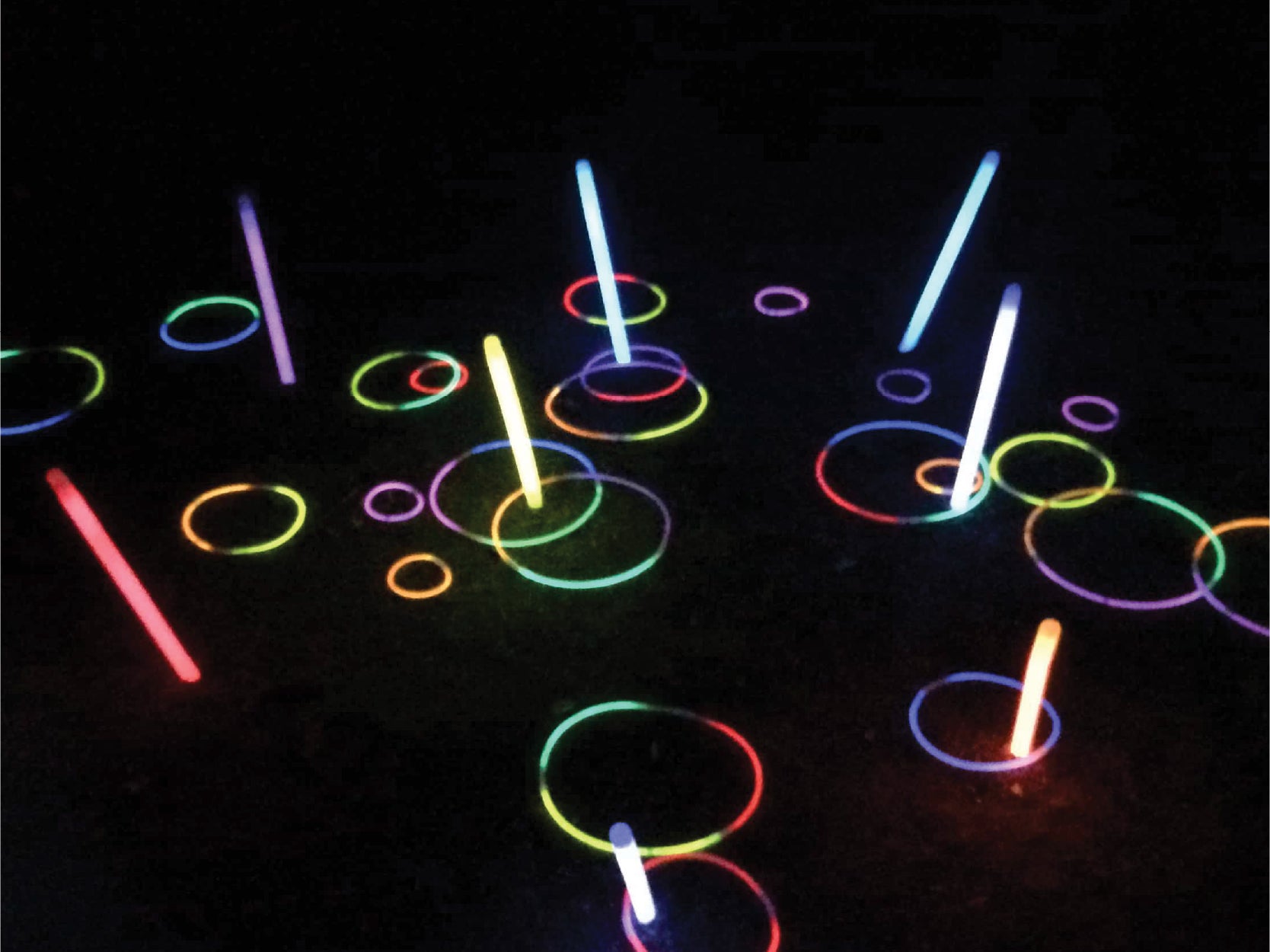 Various glow-in-the-dark rings and sticks against a dark background