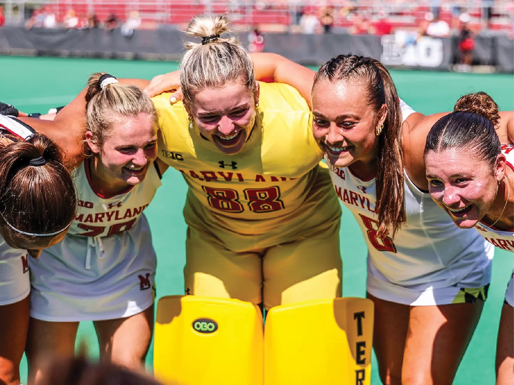 Five members of the Maryland field hockey team link arms and smile