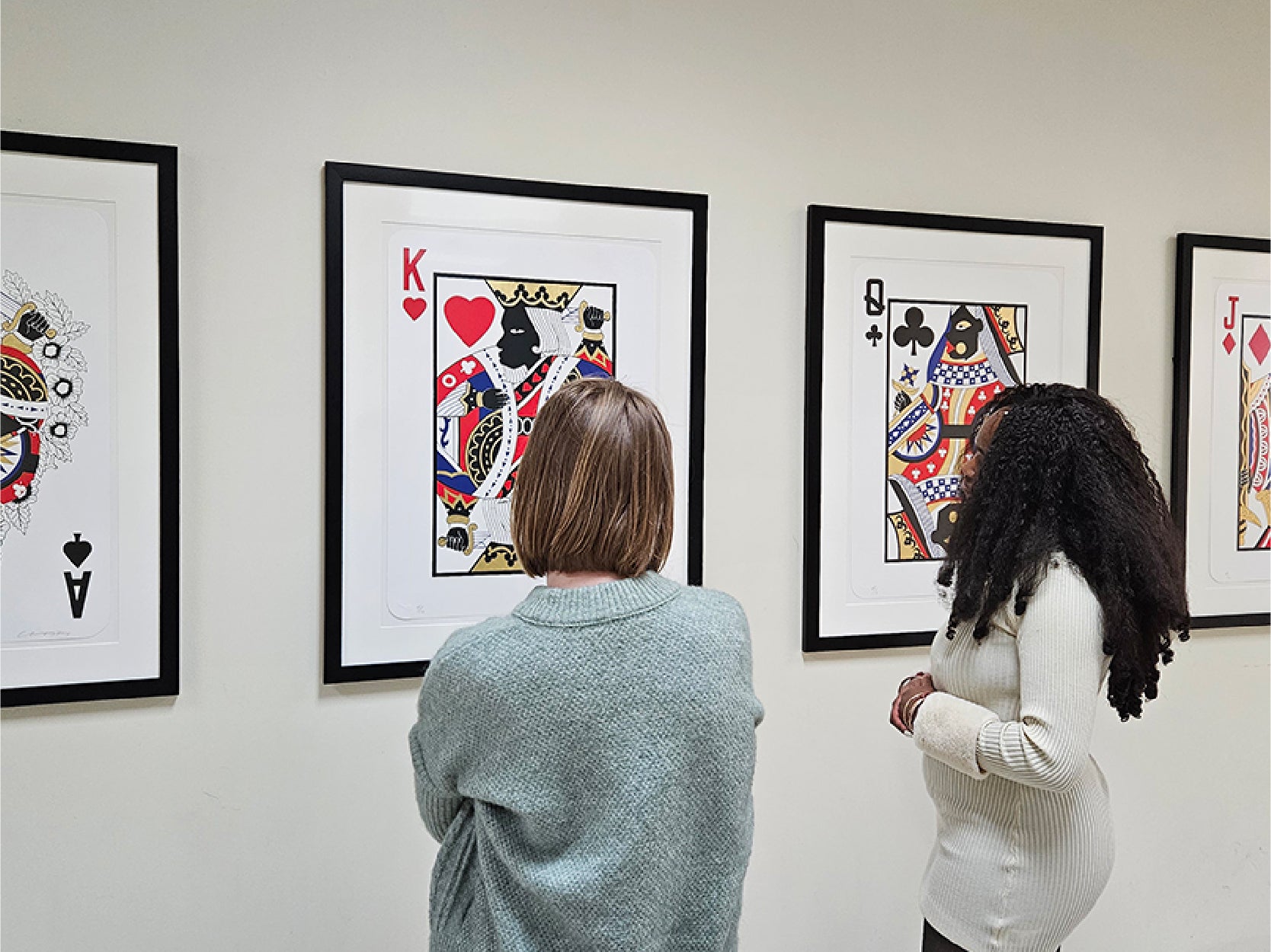 Two women look at a series of art pieces displayed on the walls of STAMP