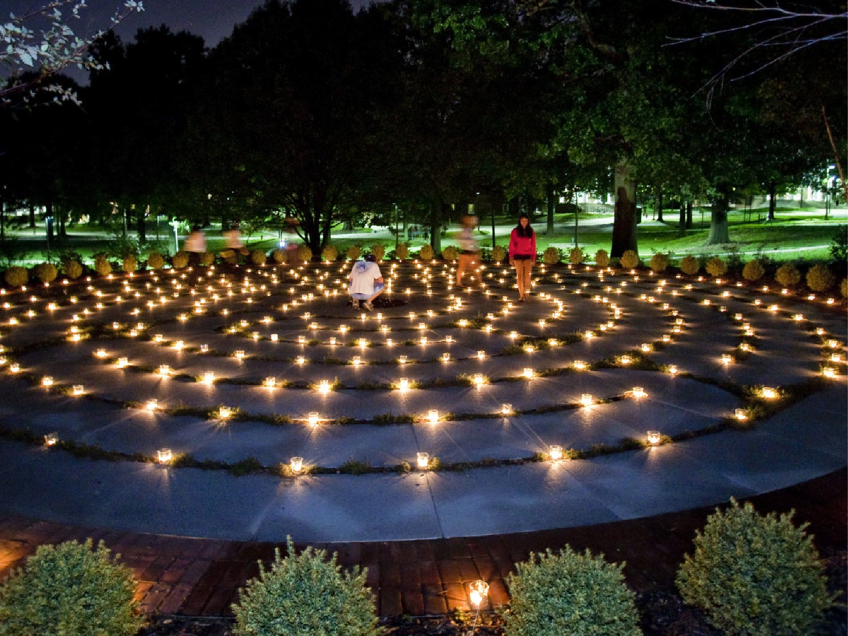 People walk on the UMD Memorial Chapel Labyrinth at night, with small candles illumiating the path