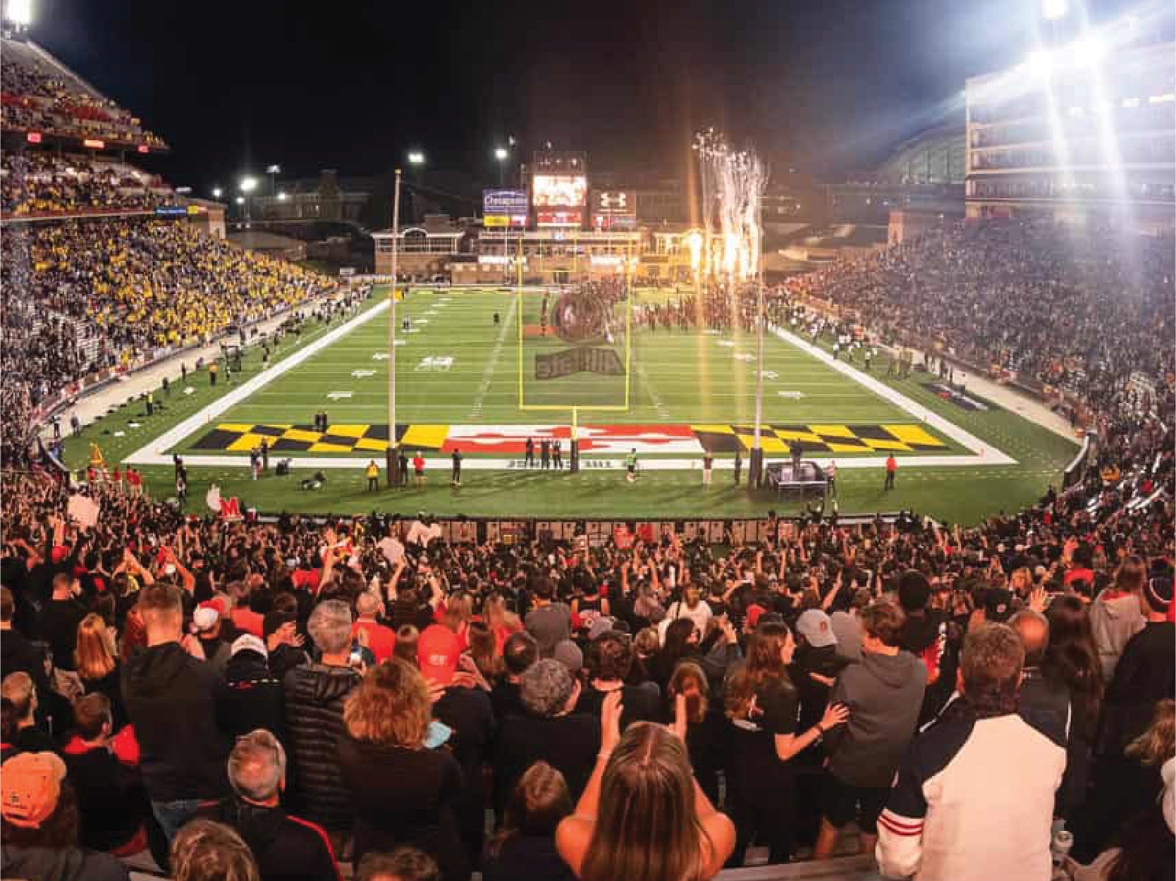 Crowds of spectators look down onto UMD's football field as fireworks go off and players run onto the field
