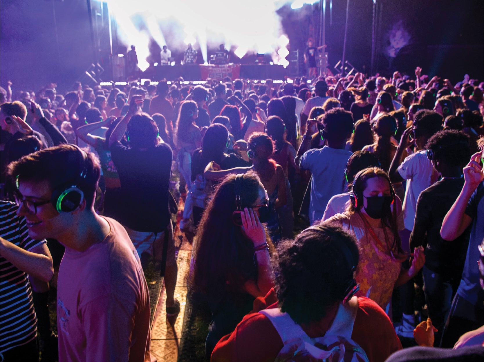A large group of UMD students dance in front of a stage while wearing headphones