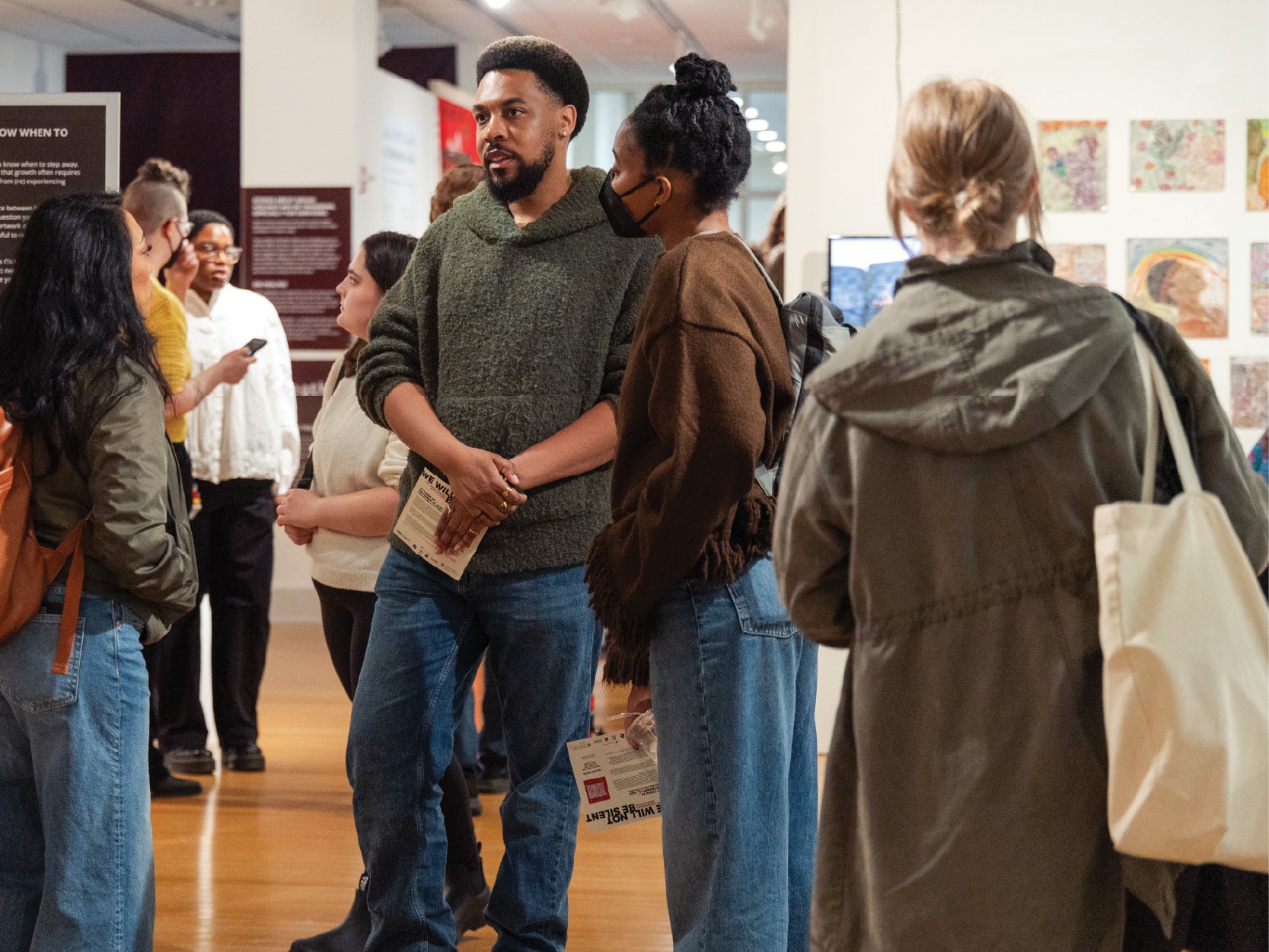 A group of UMD community members stand and converse in front of artwork in the STAMP Gallery