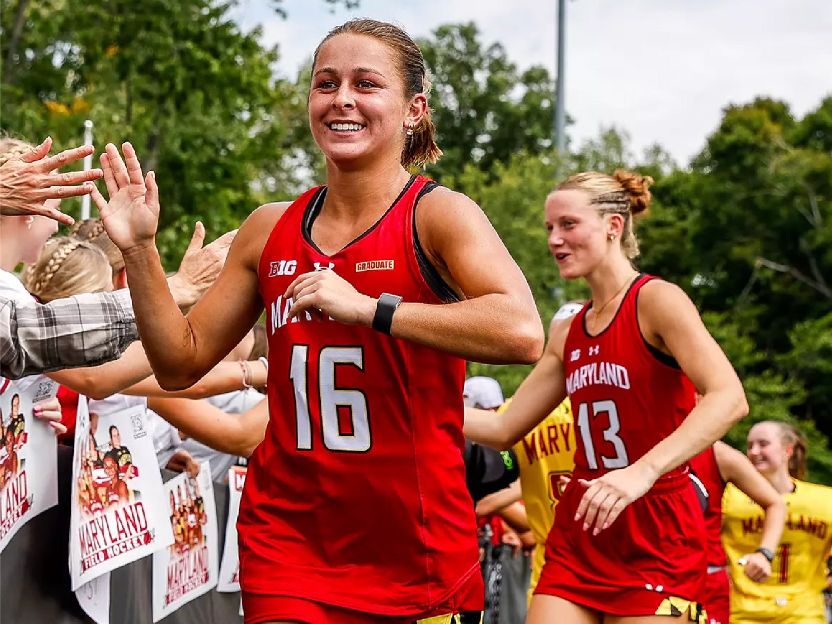 Members of the Maryland field hockey team smile while high-fiving fans