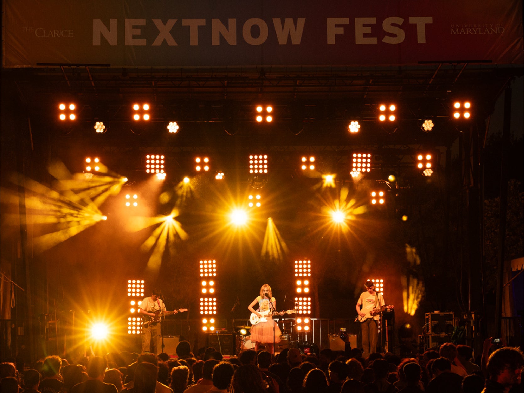 A band performs a nighttime concert below a "NextNOW Fest" banner for a large audience