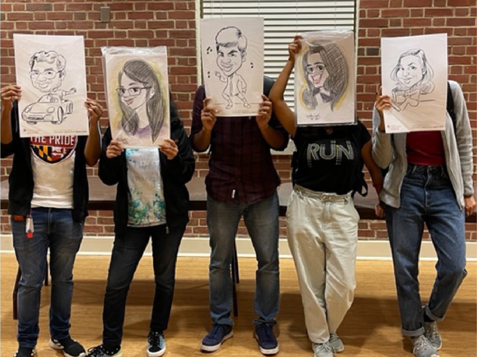 A photo of five students holding up caricature projects covering their faces.