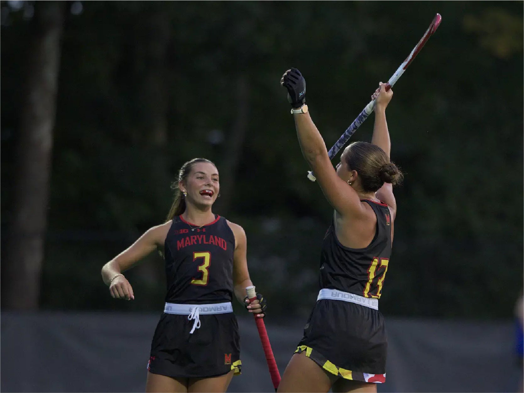 A photo of two UMD Fied Hockey players during an evening game.