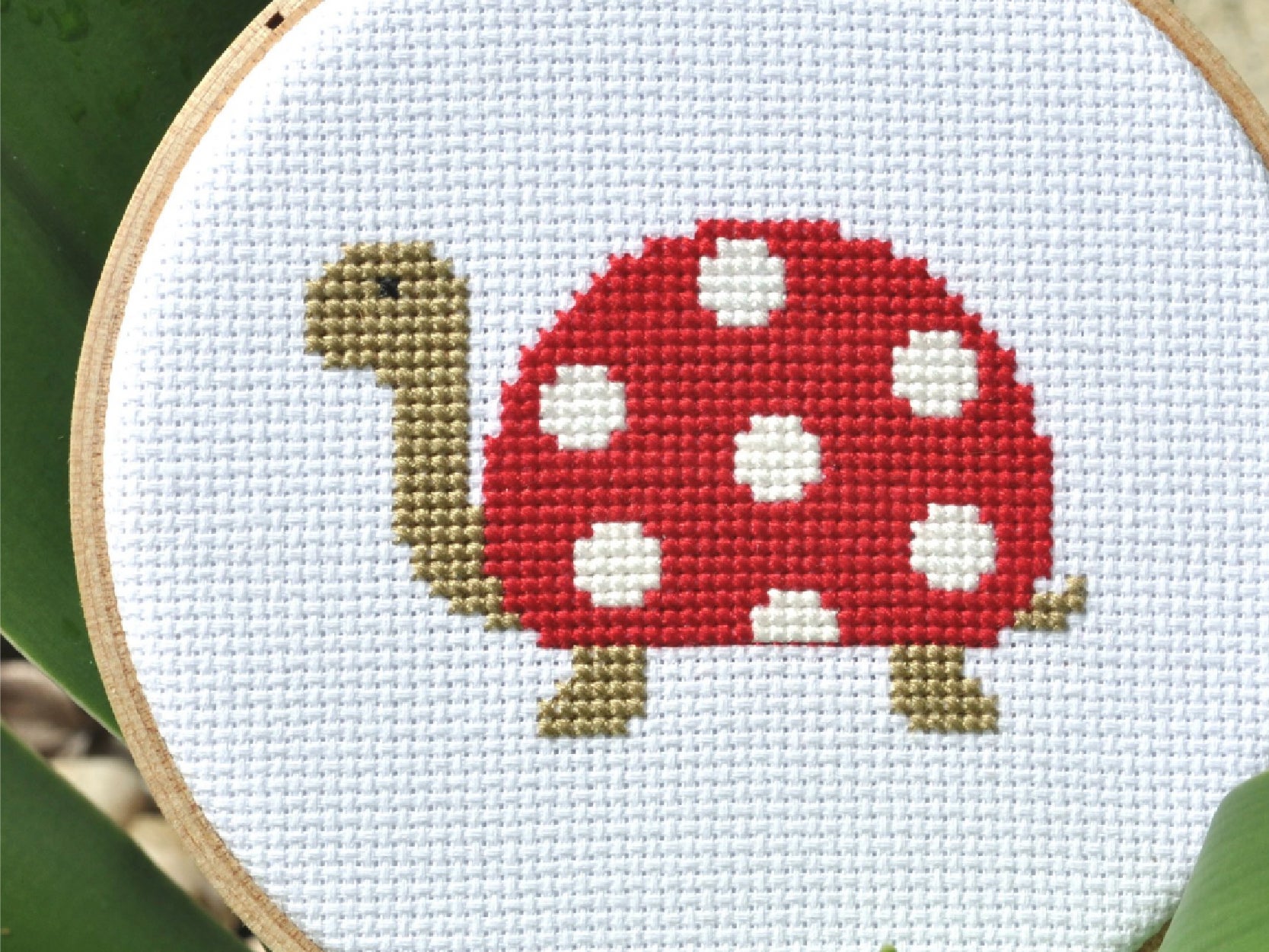 An photo of a cross stitch project of a turtle with a red and white shell.