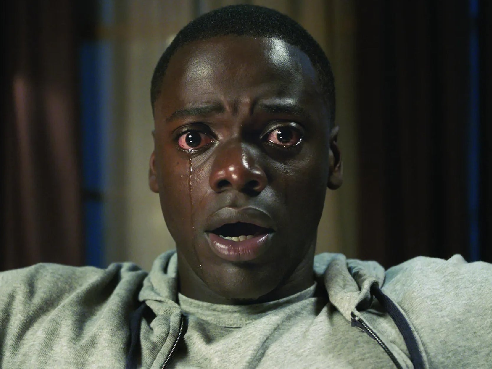 A promotional image from the movie "Get Out". It is a photo of the main character with a shocked expression with tears coming out of his eyes.