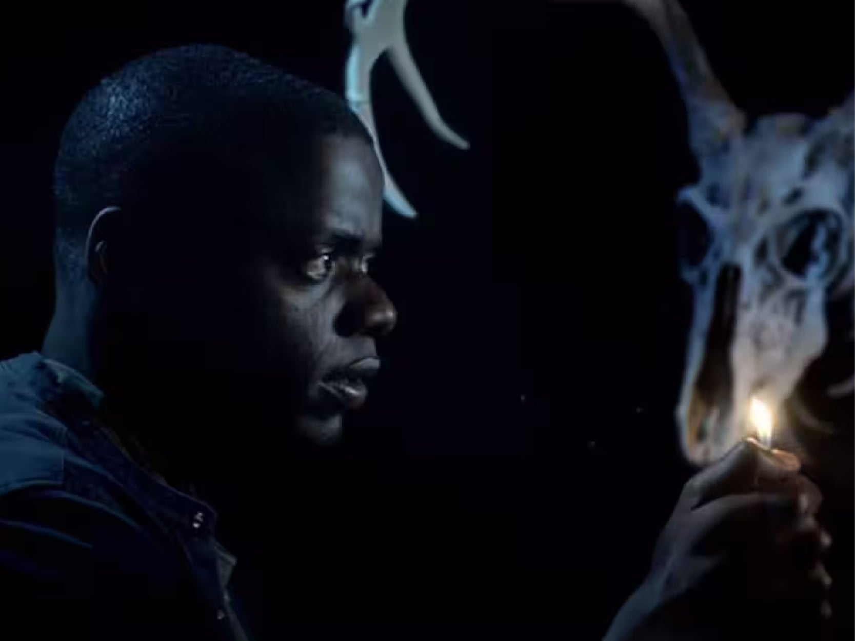 A promotional image from the movie "Get Out". It is a dark background with the main character holding a lighter. 