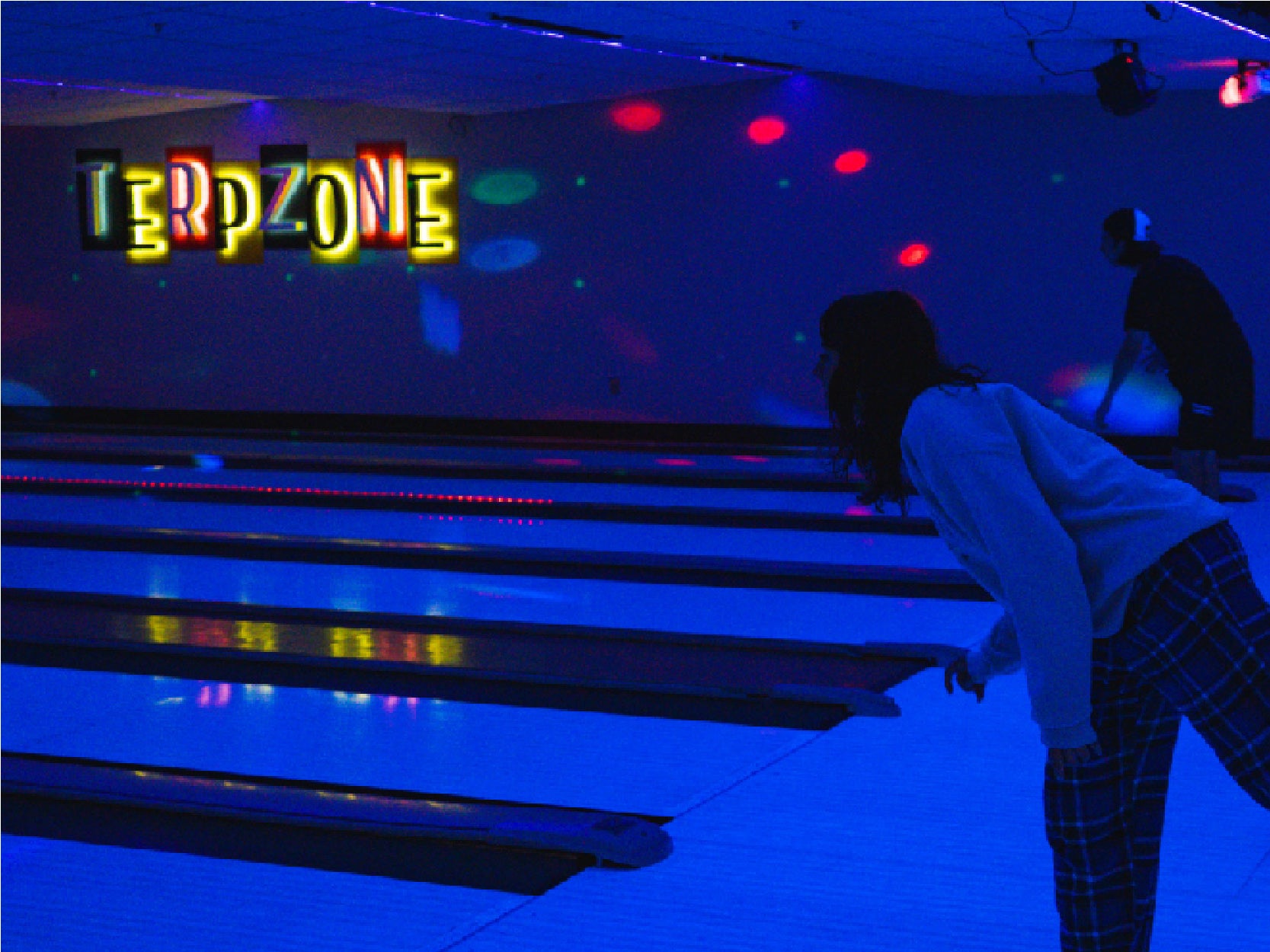 A photo of two students bowling in TerpZone during a Glow Bowling light.