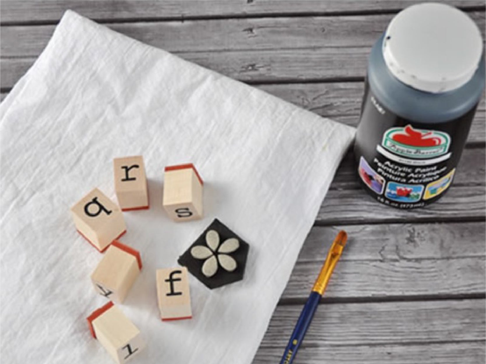 A photo of stamps, a paint brush and a bottle of black paint laif out on a gray wooden surface.